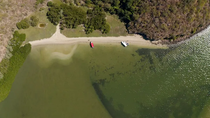 Vista aérea cenital de una playa pequeña con dos pangas varadas, rodeada de monte y manglar