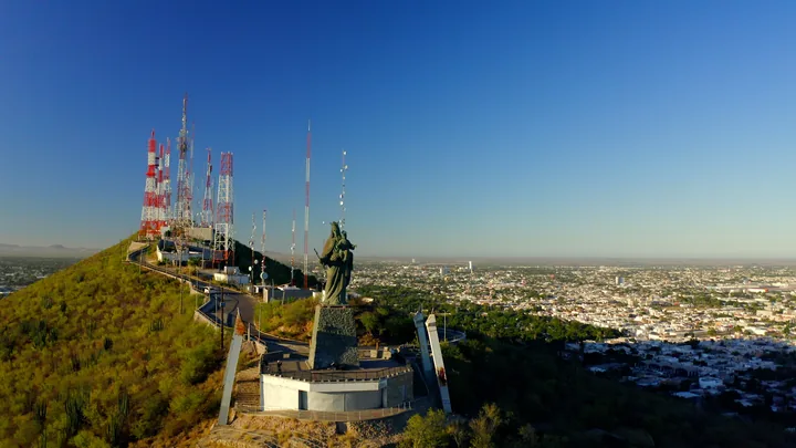 Vista aérea de un mirador en la cima de un cerro con la estatua de la Virgen del Valle, antenas de telecomunicación y la ciudad al fondo