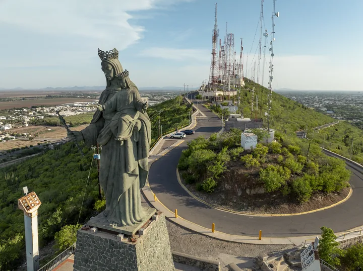 Vista aérea del Cerro de la Memoria: la estatua de la Virgen con el Niño sobre su base de piedra, el camino de acceso y las antenas de telecomunicación en la cima