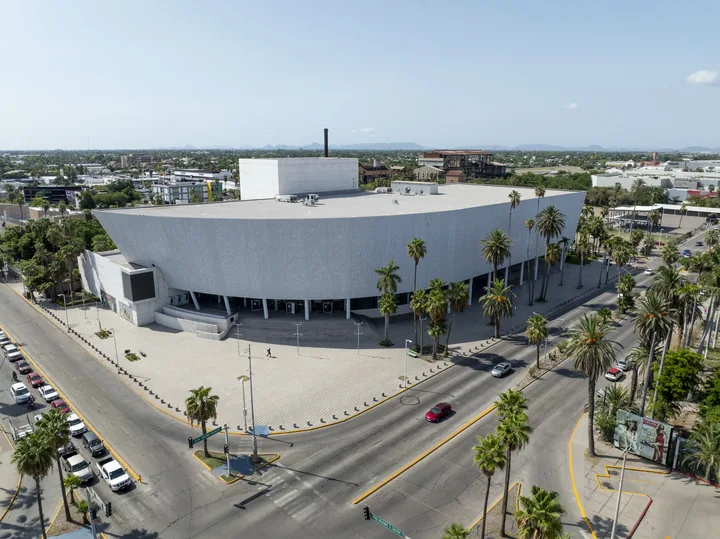 Vista aérea del Teatro Ingenio de Los Mochis, edificio de fachada blanca curva rodeado de palmeras, en el cruce de los bulevares Antonio Rosales y Rosendo G. Castro
