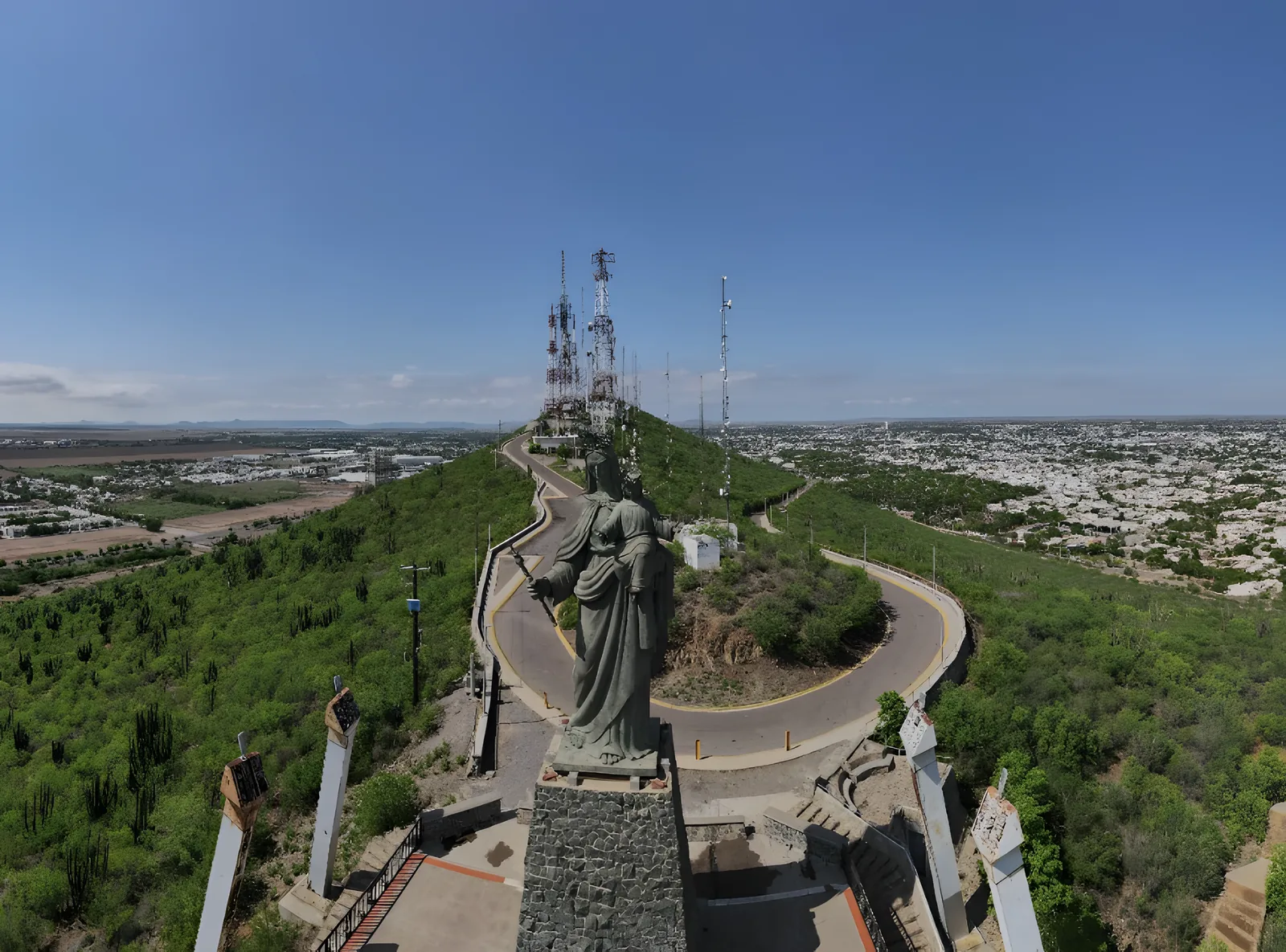 Escultura de la Virgen del Valle en la cima del Cerro de la Memoria, con el camino en curva y la ciudad al fondo